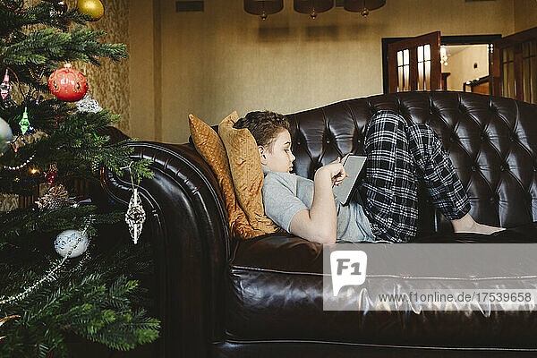 Boy using tablet PC lying on sofa at home