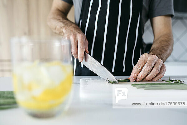 Man cutting green bean with knife on cutting board in kitchen