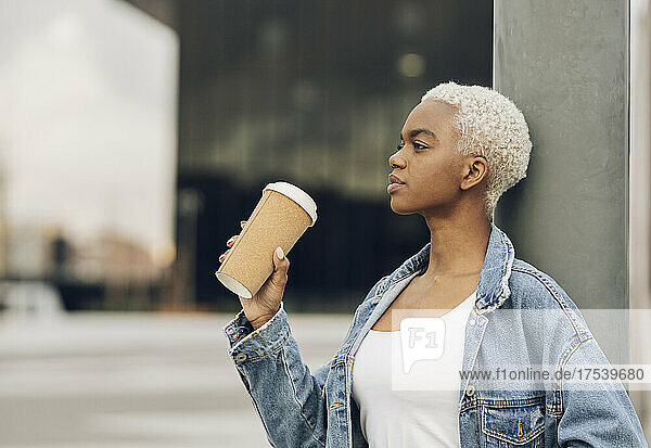 Woman holding disposable cup leaning on column