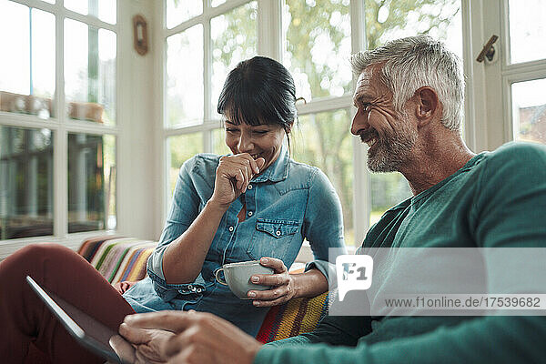 Smiling man talking with woman holding coffee cup at home