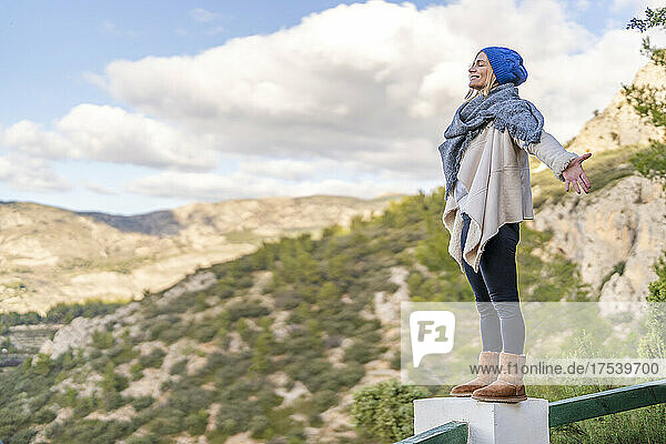Smiling woman with arms outstretched standing on railing