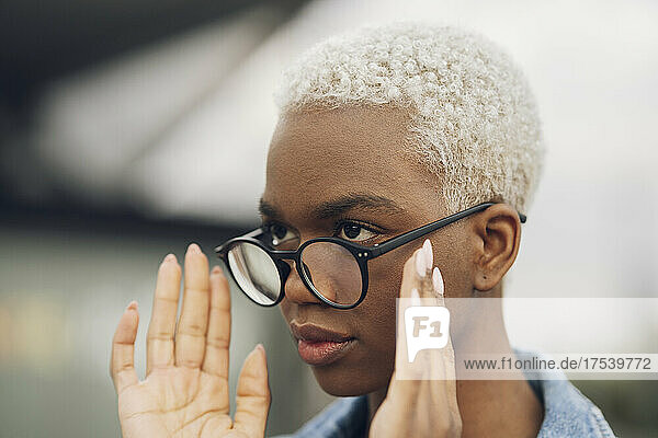 Young woman with short blond hair adjusting eyeglasses