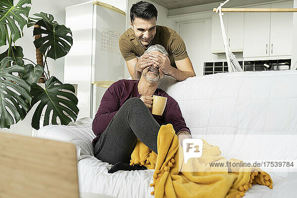 Smiling man covering husband's eyes with hands at home