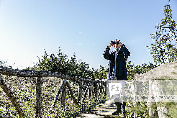 Man standing on wooden bridge looking through binoculars
