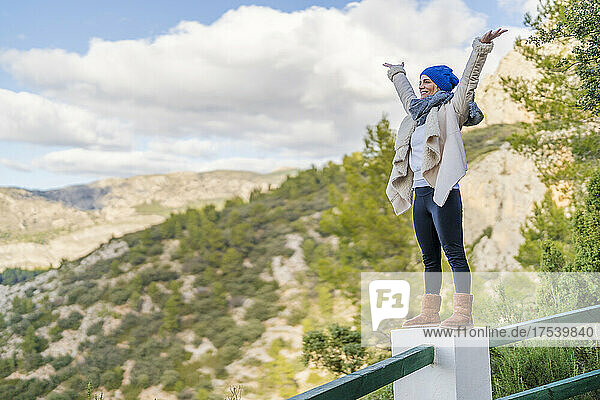 Carefree woman standing with arms raised on railing