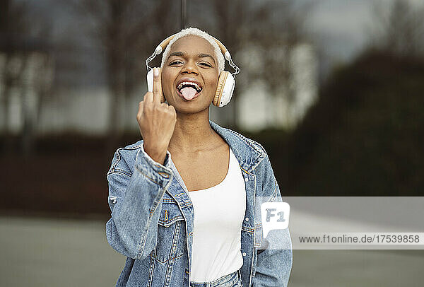 Carefree woman with headphones sticking out tongue showing middle finger