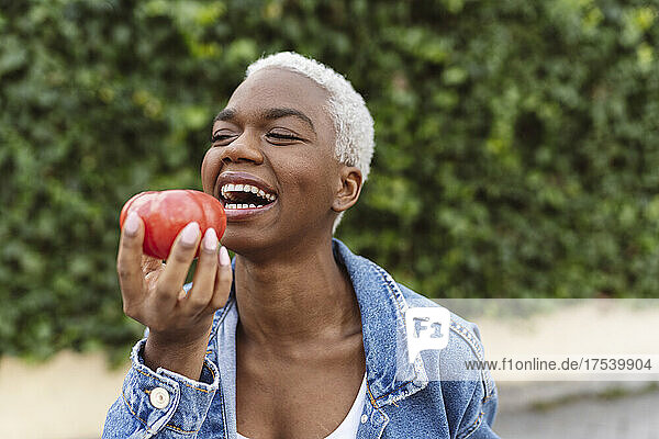 Young woman laughing holding tomato in hand
