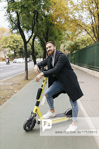 Smiling young man leaning on electric push scooter at bicycle lane
