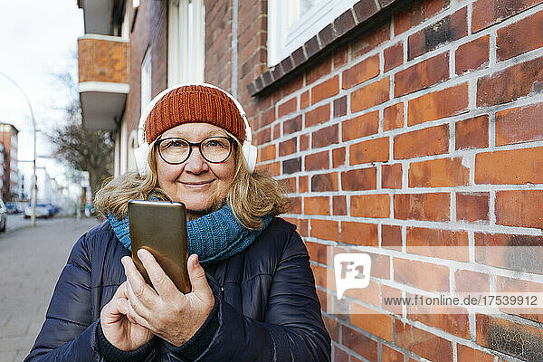 Senior woman with smart phone by brick wall