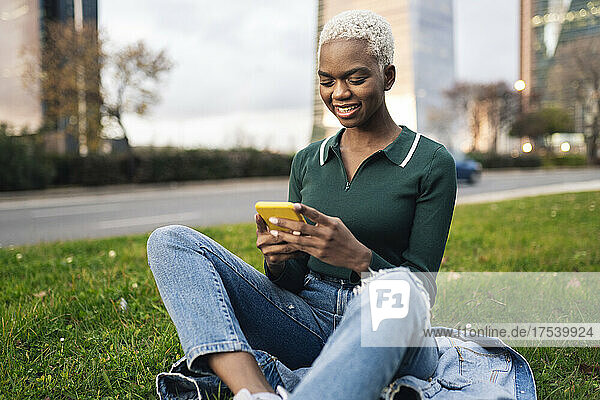 Young woman using smart phone sitting on grass at roadside