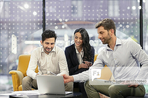 Lächelnde Geschäftskollegen diskutieren am Laptop im Büro