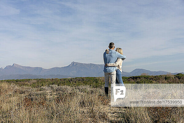 Mann und Frau schauen auf Berge und umarmen sich in Dünen