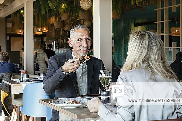 Smiling man holding sushi looking at woman in restaurant