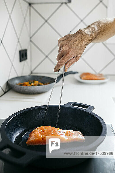 Man cooking fish with tongs in cooking pan at home