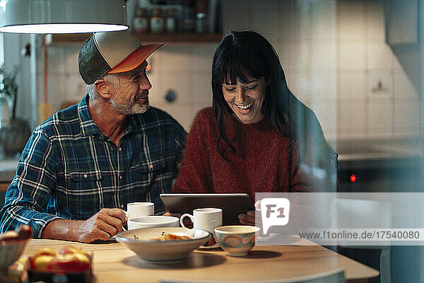 Cheerful couple using tablet PC at table in kitchen