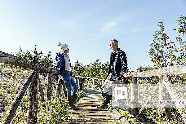 Man and woman looking at each other leaning on wooden bridge