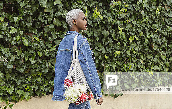 Woman walking by plants carrying groceries in mesh bag