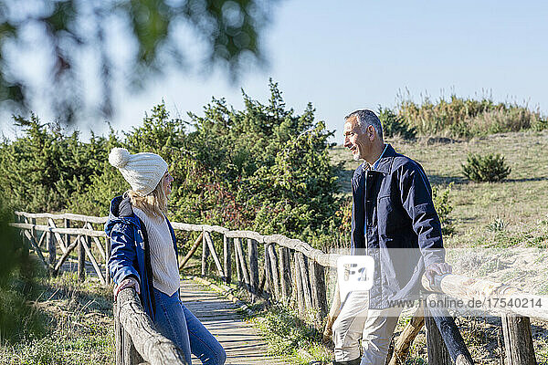 Couple talking to each other leaning on wooden bridge