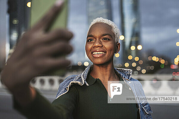 Woman taking selfie through smart phone in city at dusk