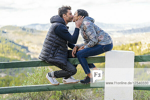 Affectionate couple kissing each other sitting on railing
