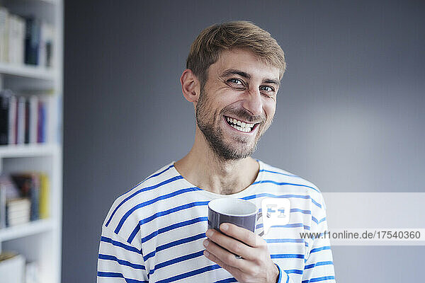 Happy man holding coffee cup at home
