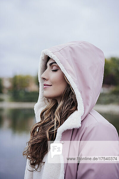 Woman with eyes closed wearing hooded jacket at park
