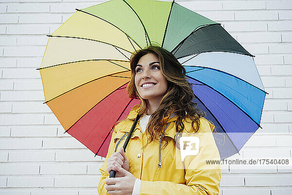 Nachdenkliche Frau hält Regenschirm vor der Wand