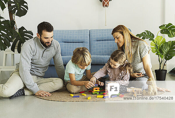 Brother and sister playing toy blocks with parents in living room