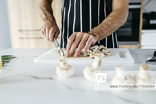 Man slicing mushroom in kitchen at home