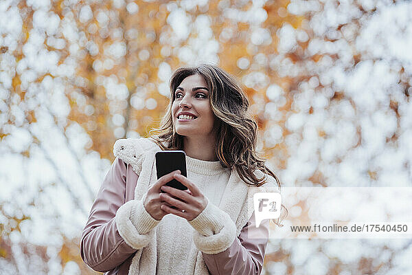 Smiling woman holding mobile phone at park