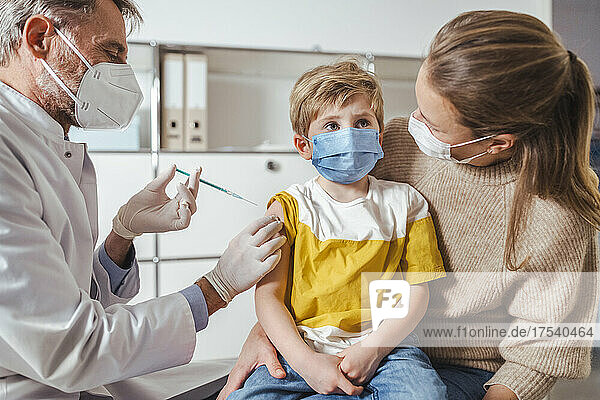 Boy being vaccinated by doctor while on lap of mother