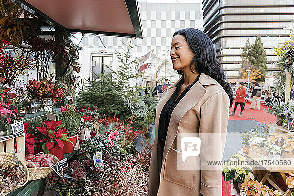 Lächelnde Frau mit Mantel im Blumenladen auf dem Weihnachtsmarkt