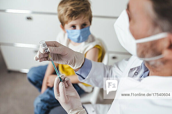 Doctor preparing vaccine injection for boy in background at center