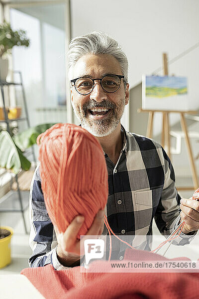 Smiling man with eyeglasses showing wool at home