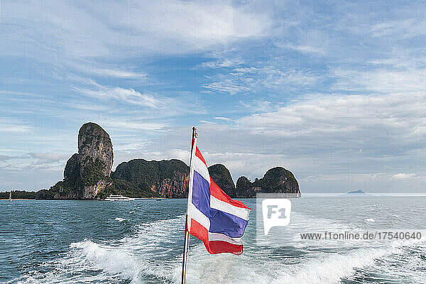 Thailändische Flagge über dem Kielwasser des Bootes auf See unter bewölktem Himmel