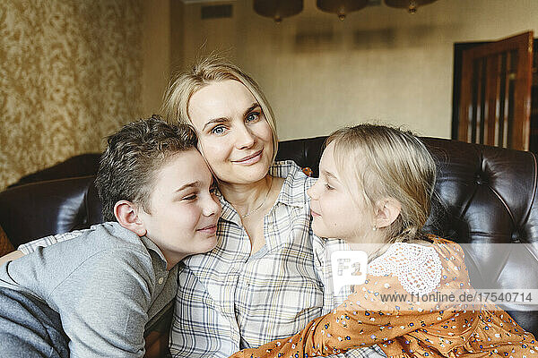 Lächelnde Mutter mit Tochter und Sohn  die zu Hause auf dem Sofa sitzen