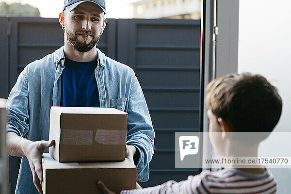 Young delivery man giving packages to boy at home