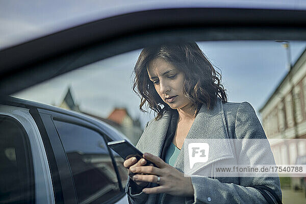 Woman using mobile phone at open car door
