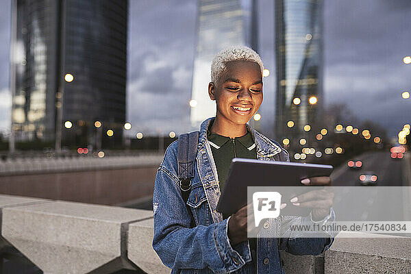 Smiling woman using tablet PC standing on bridge in city