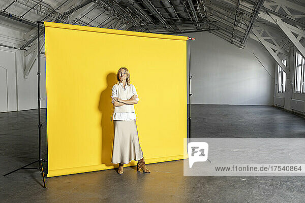 Confident businesswoman with arms crossed standing in front of yellow backdrop