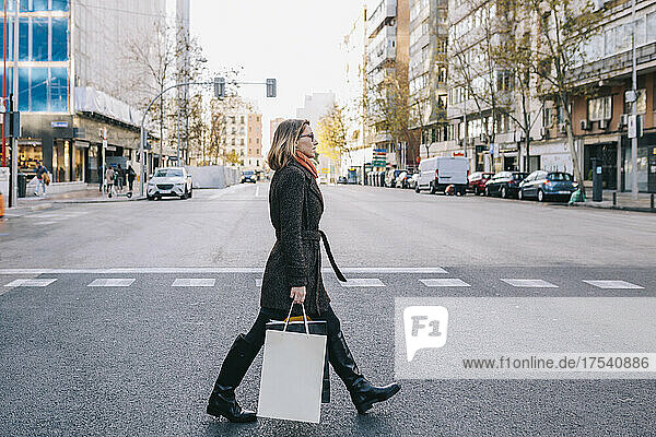 Woman with shopping bags crossing road in city