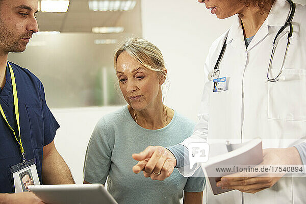 Senior patient looking at tablet PC by healthcare workers in medical room