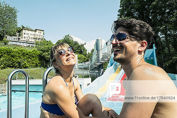 Happy couple sitting together at swimming pool