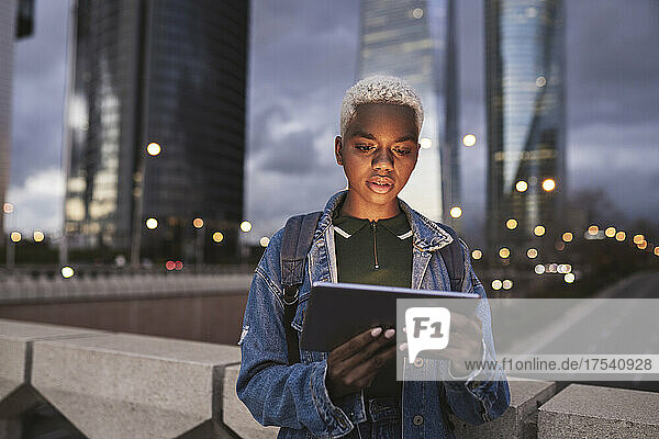Woman with tablet PC standing on bridge in city at dusk