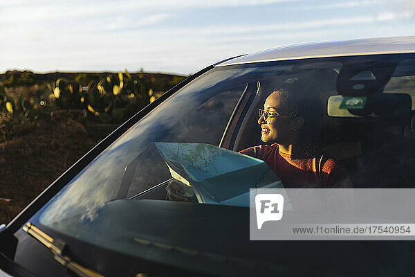 Lächelnde Frau sitzt bei Sonnenuntergang mit Karte im Auto