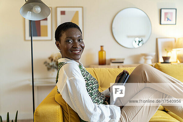 Happy woman with tablet PC on sofa at home