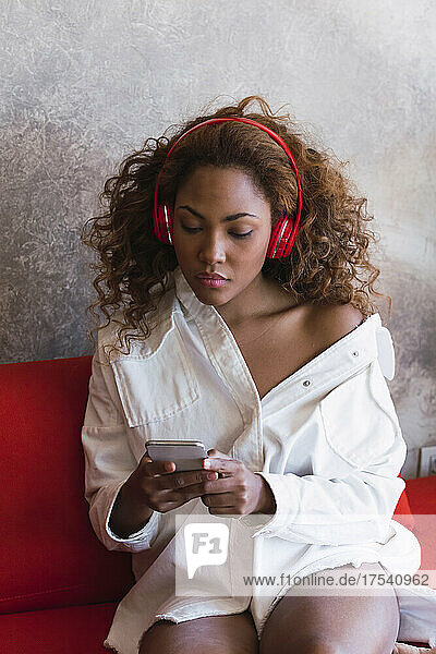 Woman with wireless headphones using mobile phone on sofa