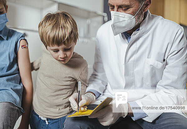 Doctor filling vaccination certificate with boys at center