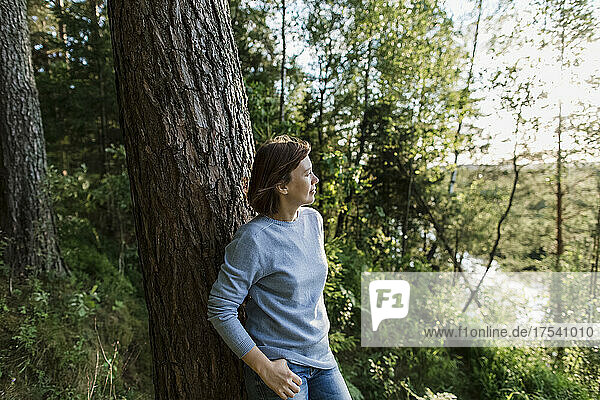 Thoughtful woman leaning on tree