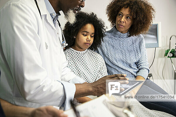 Frau und kranke Tochter schauen sich Arzt an  der Bericht auf Tablet-PC im Krankenhaus teilt